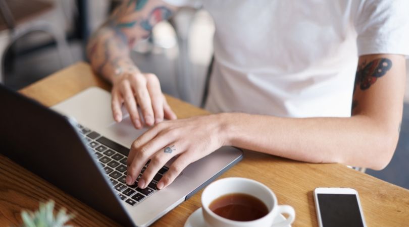 man with tattoos typing on a computer