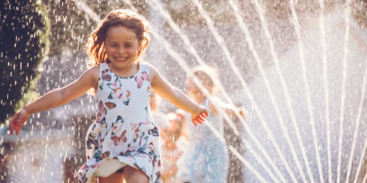 little girl running through a sprinkler